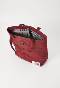 Bolsa de tela roja con asas dobles, interior gris y un pequeño acento de diamante. Presenta el logo de The North Face en el lateral.