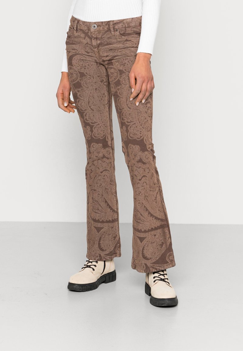 Bruna utsvängda jeans med paisley-mönster, mjuk textur, fem fickor och en subtil lyster, kombinerade med beige snörade ankelstövlar.