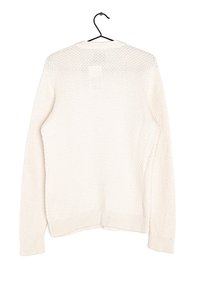 Ljusbeige stickad tröja med en texturerad, våffelmönster, långa ärmar samt ribbade mudd- och nederdelar. Visas hängande på en svart krok.