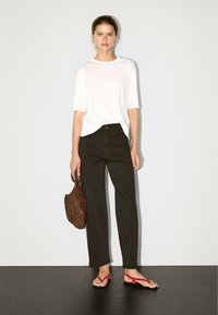 White short-sleeve top, high-waisted black wide-leg pants, red flip-flops, and a textured brown woven bag. Simple, minimal design.