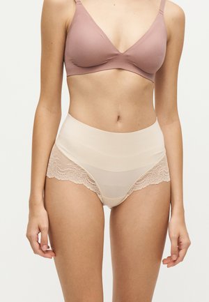 Femme portant un soutien-gorge mauve et un slip taille haute beige orné de dentelle, montrée des épaules jusqu'aux cuisses sur un fond uni.