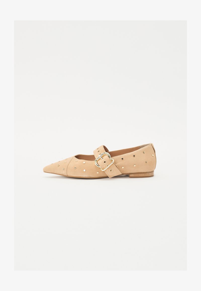 Zapato plano beige con punta afilada, material de ante, tachuelas doradas decorativas y una correa en el tobillo con un detalle de hebilla redonda.