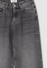 Jeans in denim grigio scuro con una texture scolorita, dotati di cinque tasche, zip a bottone e rivetti in bronzo vicino alle tasche. Design pulito con gamba dritta.