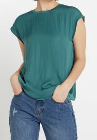 Tyrkysový krátký rukáv top z měkké tkaniny s volným střihem, kulatým výstřihem a jemně splývavým designem, v kombinaci s modrými džíny.