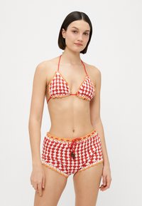 Gehaakte bikini set met een rood-wit ruitpatroon. Het bovenstuk heeft driehoekige cups, terwijl de onderkant een trekkoord in de taille en decoratieve afwerking heeft.