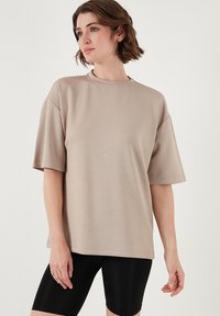 Beige oversized t-shirt med korte ærmer, rund halsudskæring, glat tekstur, parret med sorte cykelshorts. Simple, moderne design.