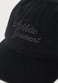 Svart baseball caps med brodert kursiv tekst "Athletic Garment" på frontpanelet, vist mot en hvit bakgrunn.