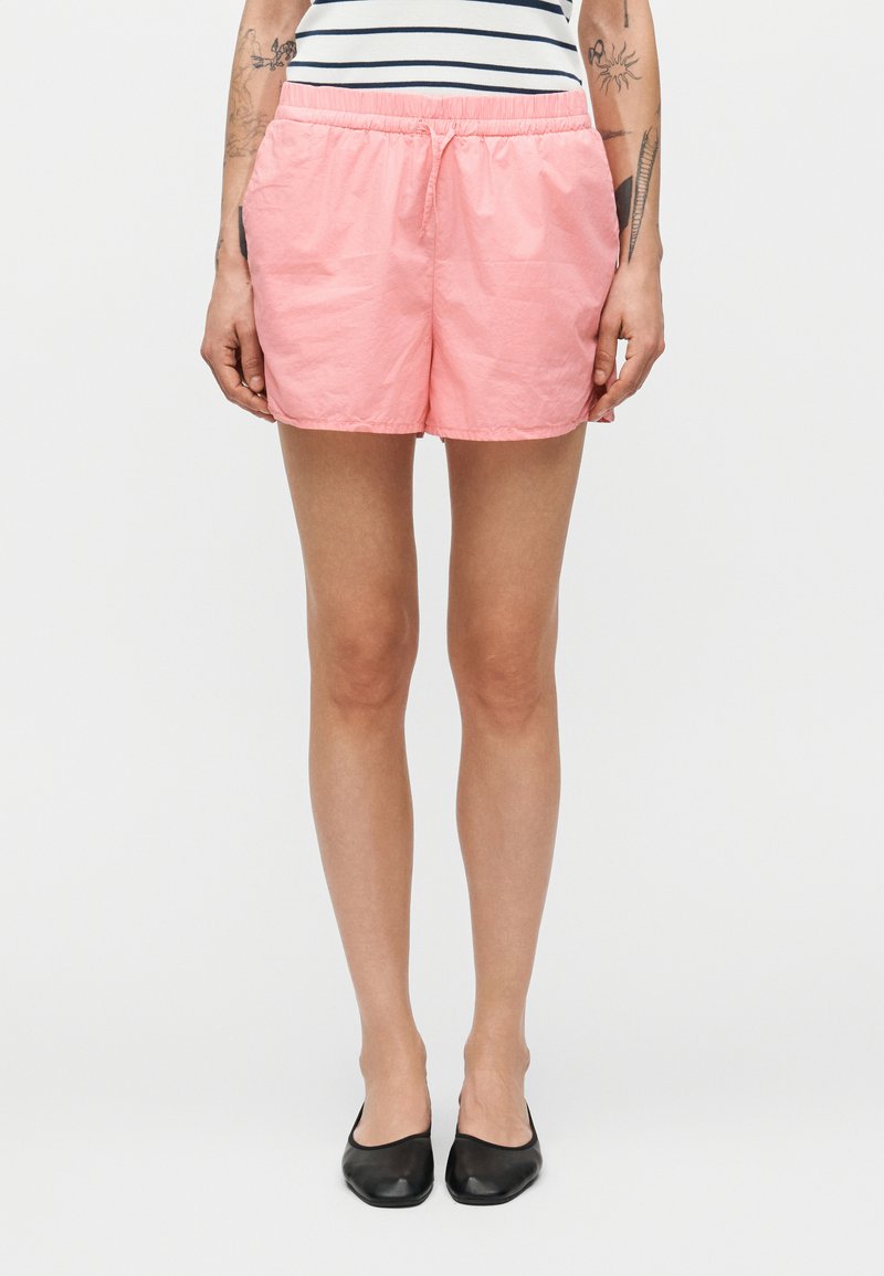 Ροζ σορτς κατασκευασμένα από ελαφρύ ύφασμα με ελαστική μέση. Ομαλή υφή, μήκος μέχρι το γόνατο, με απλό σχεδιασμό χωρίς τσέπες.