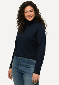 Tmavě modrý dlouhý rukávrolák s měkkou texturou, spárovaný s vybledlými modrými džíny. Jednoduchý design, žádné viditelné vzory nebo kovové prvky.