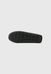 Schwarze Gummi-Schuhsohle mit strukturiertem Design, das rechteckige Muster für Grip aufweist und ein Logo an der Seite hat. Insgesamt glatte Oberfläche.
