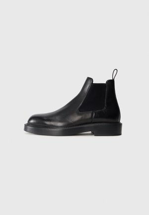 Schwarze Leder-Chelsea-Boots mit elastischen Seitenpanelen, runder Zehenform, flacher Gummisohle und einer Zuglasche auf der Rückseite. Glatte Textur.