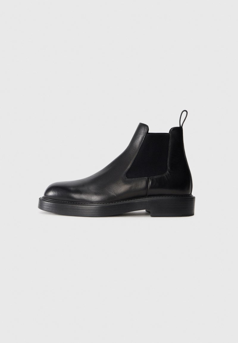 Svarta läder Chelsea-boots med elastiska sidopaneler, rundad tå, platt gummisula och en dragflik baktill. Slät yta.