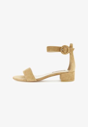 Beige ruskind sandal med blokhæl og ankelrem, der har en cirkulær spænde og et minimalistisk design. Glat overflade, åben tå.