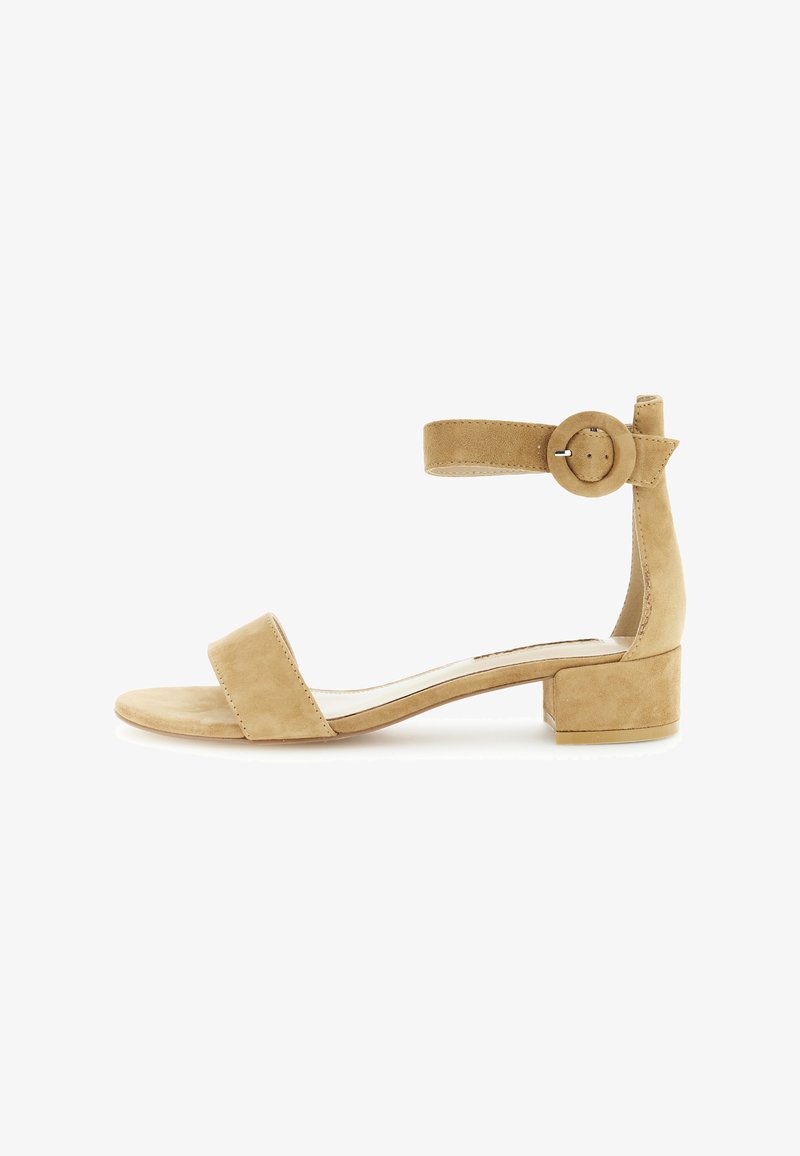 Beige ruskind sandal med blokhæl og ankelrem, der har en cirkulær spænde og et minimalistisk design. Glat overflade, åben tå.