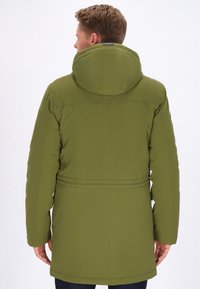 Veste matelassée vert olive avec capuche ajustée, taille élastique et manches longues. Étiquettes amovibles visibles au niveau du col arrière.