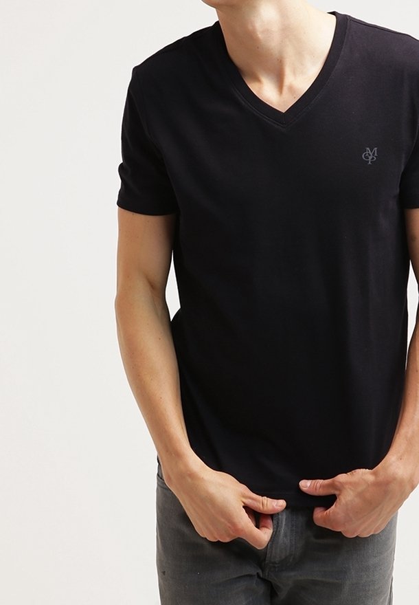 Homme portant un t-shirt noir ajusté à col en V et manches courtes, avec un petit logo sur le côté gauche de la poitrine, ajustant l'ourlet par-dessus un pantalon foncé.