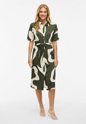 Knielanges Hemdkleid in Dunkelgrün und Creme mit abstrakten Wellenmustern. Mit einem Gürtel in der Taille und kurzen Ärmeln, aus strukturiertem Stoff gefertigt.