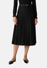 Gonna plissettata nera con vita aderente, dotata di una cintura nera slim con accessori metallici. Il tessuto strutturato aggiunge profondità e forma.