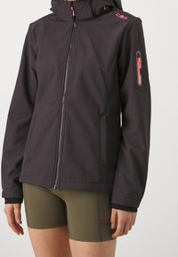 Veste imperméable noire à coupe ajustée, fermeture éclair frontale, capuche et accents roses. Dotée d'une poche latérale zippée et d'un tissu texturé.