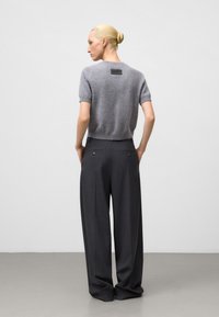 Maglione grigio a maglia con maniche corte e una piccola etichetta sul retro, abbinato a pantaloni grigi a vita alta e gamba larga con sottili dettagli metallici.
