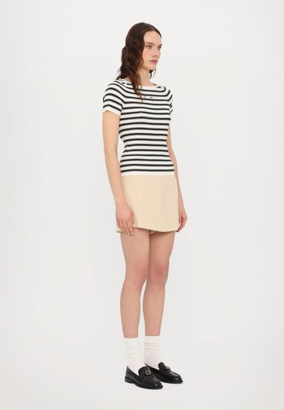 Stripet striktrøje i sort og hvid med korte ærmer, parret med en beige nederdel. Sorte loafers og hvide knæstrømper fuldender looket.