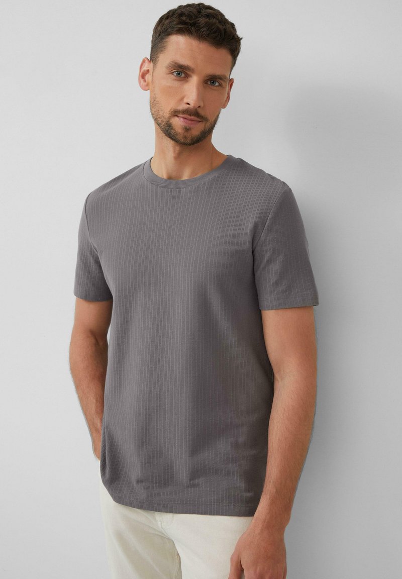 Graues, geripptes Kurzarm-T-Shirt mit Rundhalsausschnitt. Der Stoff wirkt weich und hat eine dezente Textur. Getragen mit hellen Hosen.