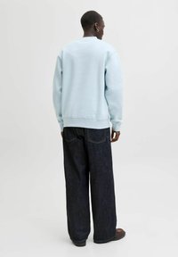 Hellblauer Pullover mit lockerem Sitz, gerippten Bündchen und Saum, kombiniert mit dunkelblauen Jeans mit weitem Bein. Schlichtes Design, keine sichtbaren Muster oder Logos.