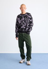 Pulover negru cu un model abstract violet, pantaloni din fetru verde măsliniu și adidași albi cu accente bej. Croială simplă, lejeră.