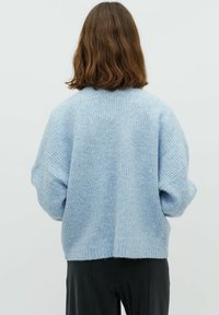 Suéter de punto azul claro con un corte relajado, textura de canalé, hombros caídos y un dobladillo cortado, combinado con prendas oscuras.
