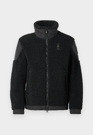 Giacca in pile nera con collo alto, chiusura con zip e dettagli in tessuto nero a contrasto su spalle e polsini. Presenta una superficie morbida e strutturata.