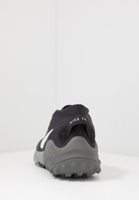 Zwarte en grijze Nike trailrunning schoen met wit logo, bekeken vanaf de achterkant die de gestructureerde zool en de trekhaak met branding toont.
