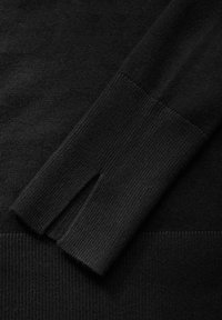 Svart stickad tröja med detaljer som visar en ribbad manschett med en skåra och en slät textur på kroppen, vilket framhäver de kontrasterande ytorna.