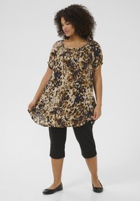 Tunique à motifs léopard avec un décolleté arrondi, des manches courtes et une silhouette fluide, associée à un pantalon capri noir et des ballerines.