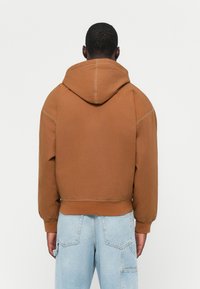 Brun hættebluse med en cropped design, synlige syninger og ribbede manchetter, parret med lyseblå denim bukser.