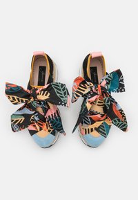 Chaussures en toile noire avec des nœuds en tissu à motifs de feuilles multicolores, des bouts en daim bleu clair et une semelle intermédiaire en jute tressé.