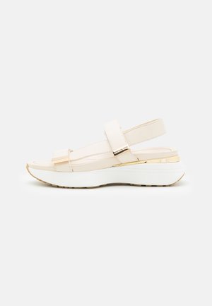 Sandale beige en cuir à bride arrière avec des sangles en Velcro, semelle rembourrée et plateforme blanche avec un accent doré sur le talon.