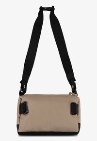 Sac rectangulaire beige avec un extérieur texturé, une base noire et une sangle noire ajustable. Présente des clips latéraux et un design minimaliste.