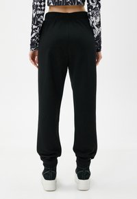 Schwarze Jogginghosen mit elastischem Bund, schmal zulaufenden Bündchen und einem weichen Baumwollmix, kombiniert mit weißen Plateausneakern.