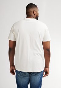 Camiseta blanca de algodón con mangas cortas, cuello redondo y un corte relajado, combinada con jeans de denim azul. La vista posterior muestra una textura suave.