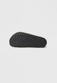 Sneakersohle mit einem schwarzen strukturierten Gummidesign, das ein wellenförmiges Muster aufweist. Das Profil ist verjüngt mit einem beigen Akzent nahe der Oberseite.