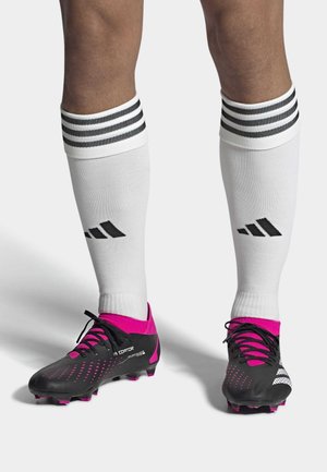 Svarta fotbollsdojor med rosa detaljer och texturerad överdel. Vita strumpor med tre svarta ränder. Nära bild av fötterna som visar skorna och strumporna.