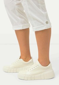 Baskets plateforme blanches avec une finition texturée, nez arrondi et rainures horizontales sur la semelle pour une meilleure adhérence. Pantalons blancs roulés visibles.