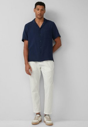 Marineblauw overhemd met korte mouwen en een gestructureerde stof, gecombineerd met lichtgekleurde, taps toelopende broek en beige sneakers met witte accenten.