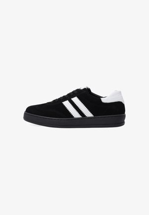 Zwarte suède sneakers met witte leren accenten, voorzien van drie witte strepen aan de zijkant, een ronde neus en een platte zwarte rubberen zool.