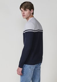 Tengerészkék kötött pulóver szürke texturált felső résszel és fehér vízszintes csíkkal. Slim fit fazon, bordázott mandzsettákkal és alsó kézel.