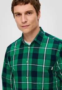 Grünes und marineblaues Karoshemd mit weißen und grauen Akzenten, ausgestattet mit einem Button-down-Kragen und einer Brusttasche mit einem kleinen Etikett.