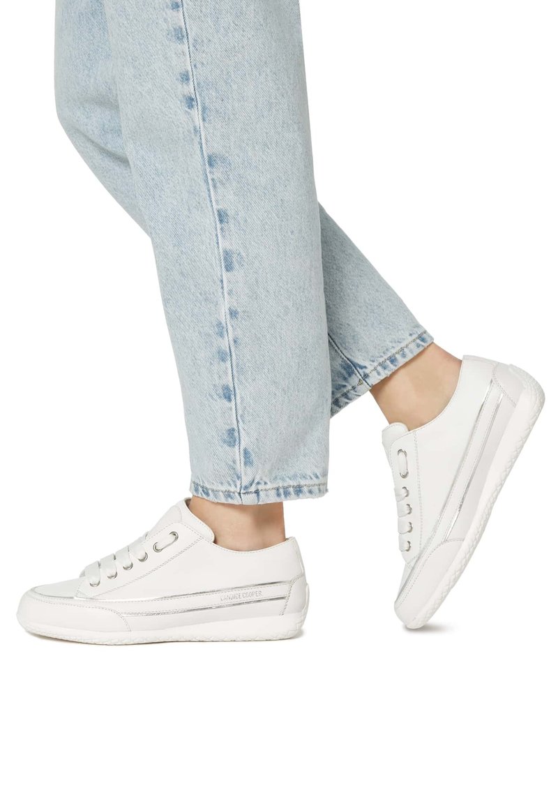 Sneaker in pelle bianca con una finitura liscia, punta arrotondata e dettagli argentati. Abbinate a jeans azzurri chiari, caratterizzati da una vestibilità comoda.