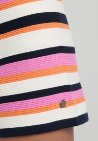 Neulehousut vaakasuorilla raidoilla vaaleanpunaisena, oranssina, valkoisena ja laivastonsinisenä. Materiaalina on tekstuuri ja siinä on pieni hopeinen logo-aksentti.