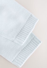 Polsini di maglione lavorati a maglia di colore azzurro chiaro, con una trama a coste, tessuto delicatamente sfumato e una superficie liscia e uniforme.