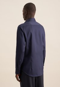 Camicia blu navy con bottoni realizzata in tessuto liscio, dotata di colletto a punta, maniche lunghe e orlo curvo, con polsini bottonati.